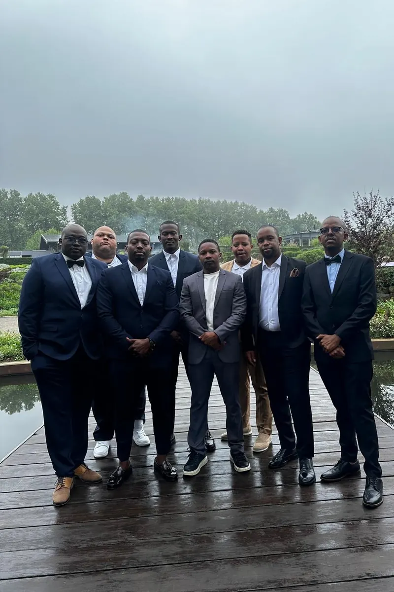 The groom&rsquo;s party in dark suits on a wooden deck under an overcast sky, raw phone photo