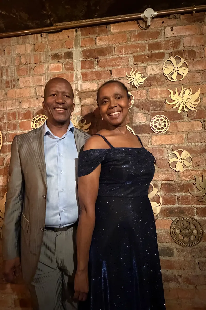 A couple posing against a brick wall at a KZN wedding reception, raw phone photo