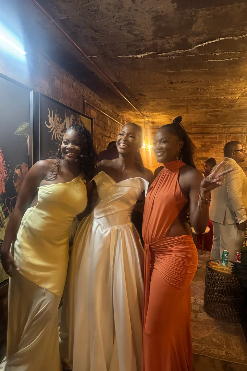 Three wedding guests in gold, champagne and rust gowns at the reception, raw phone photo