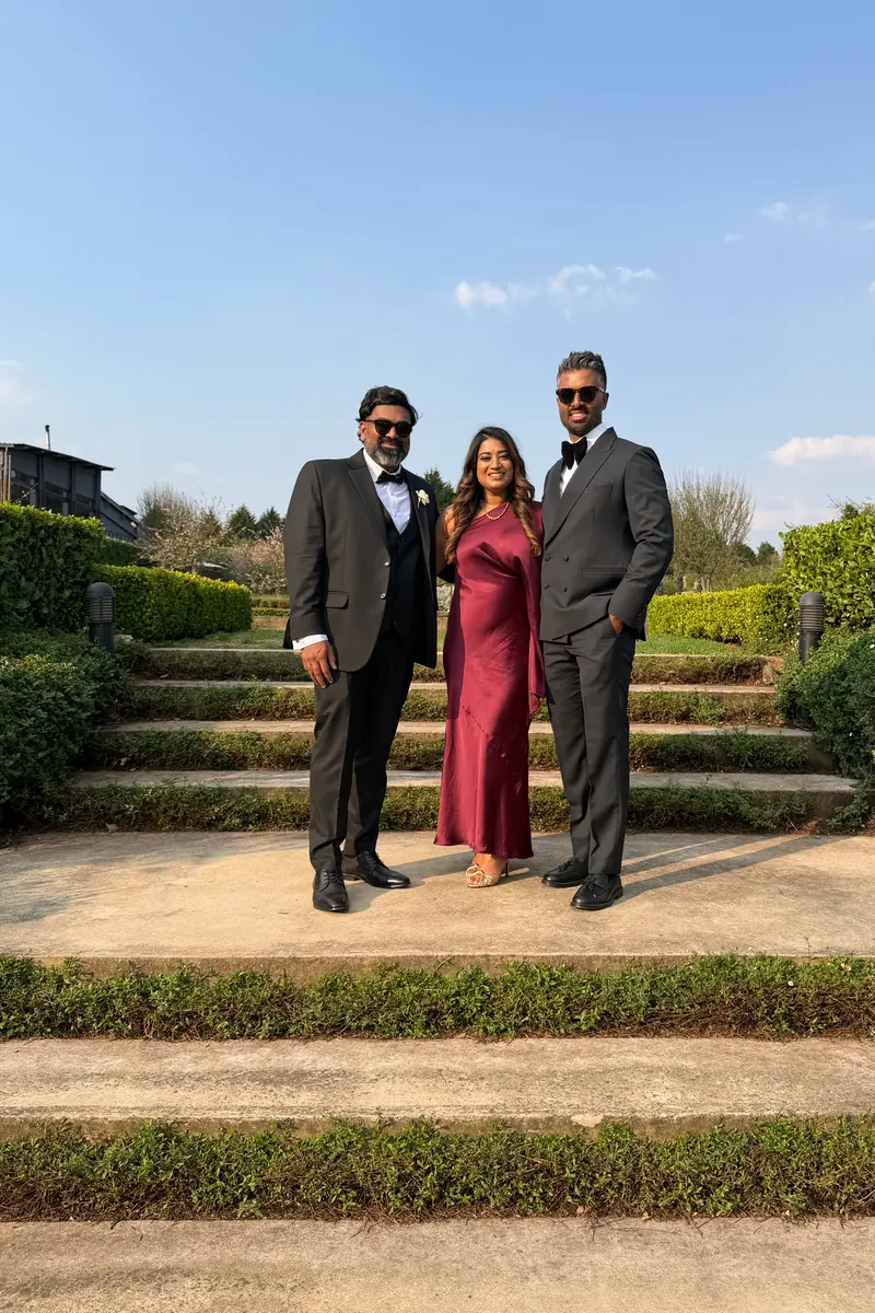 Three wedding guests in suits and a burgundy dress on garden steps, raw phone photo