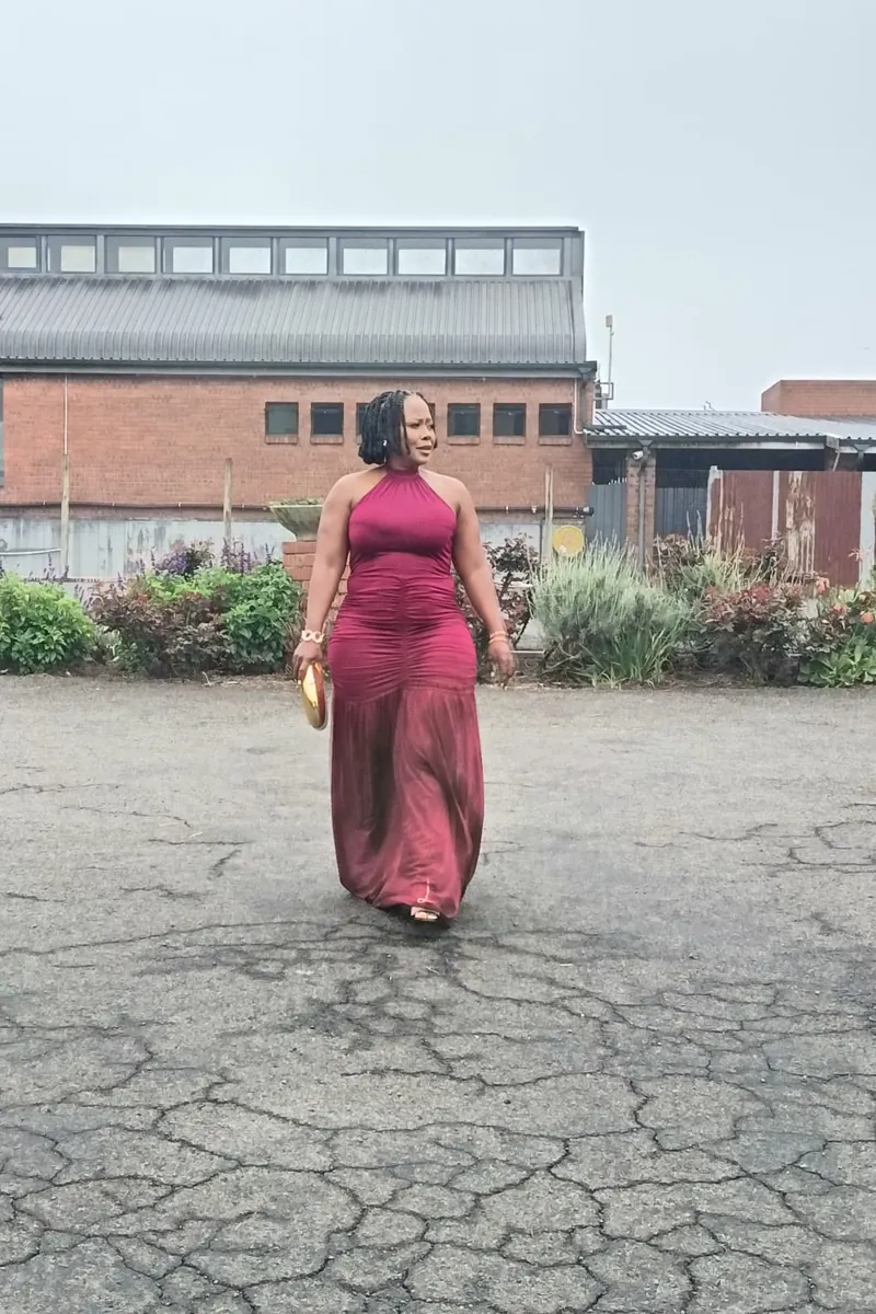 A wedding guest in a burgundy gown in a venue courtyard, raw phone photo