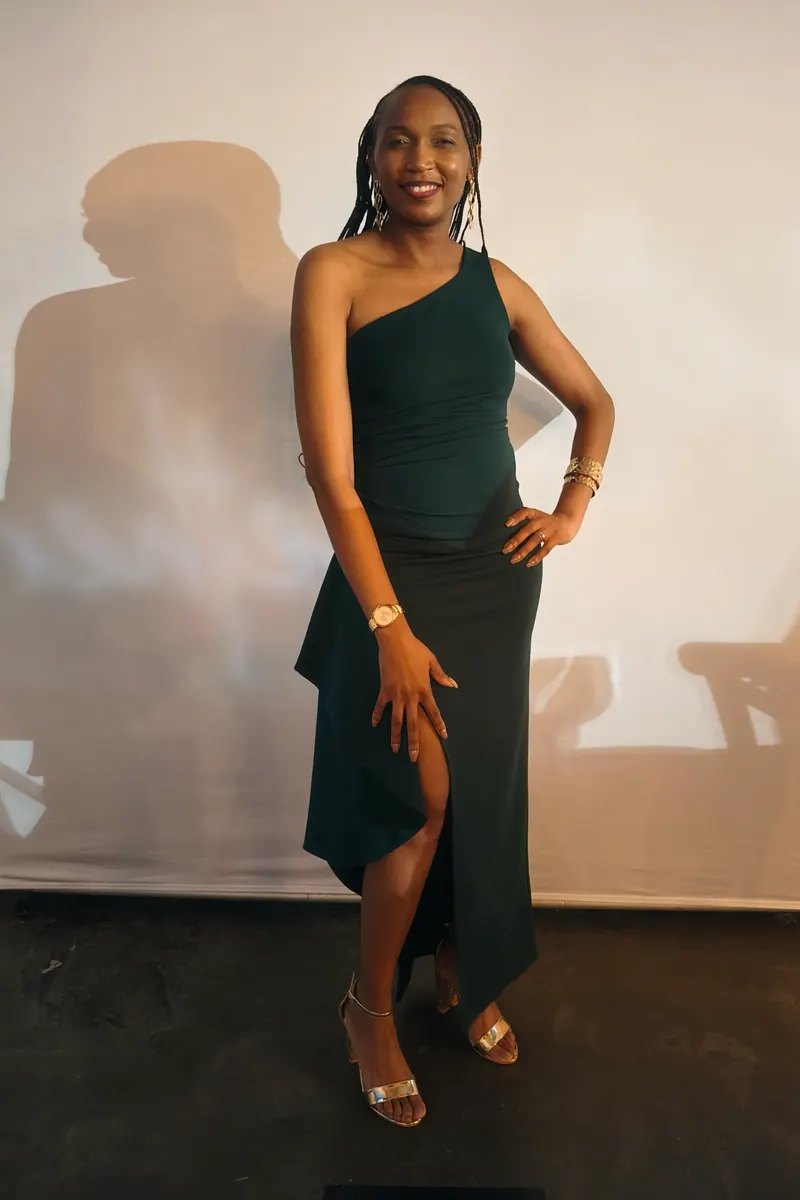 A wedding guest in a green one-shoulder dress against a plain wall, raw phone photo
