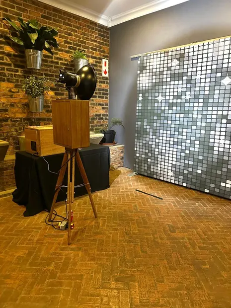 The retro photobooth beside a silver sequin wall on the brick floor at Brahman Hills