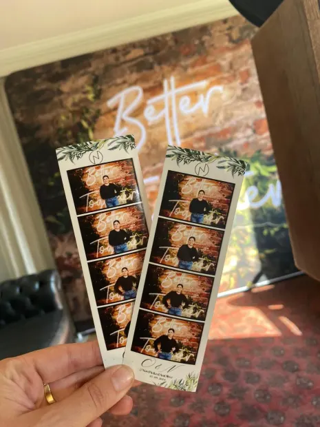 Two printed photostrips held up in front of the Better Together backdrop at Fordoun