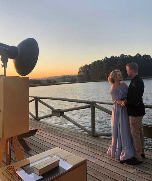 A couple on the jetty over the dam at sunset beside the photobooth at Haycroft Farm