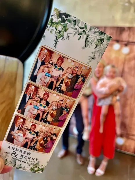 A printed photostrip from a Netherwood Farm wedding held up in front of the guests