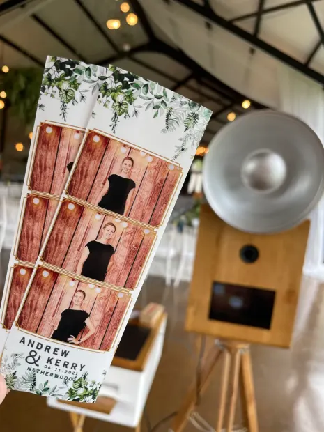 A printed photostrip held up beside the photobooth in the reception venue at Netherwood Farm