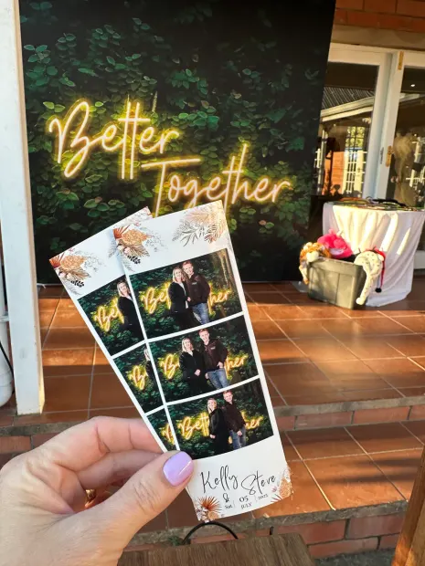 Printed photostrips held up in front of the Better Together neon at a Providence wedding