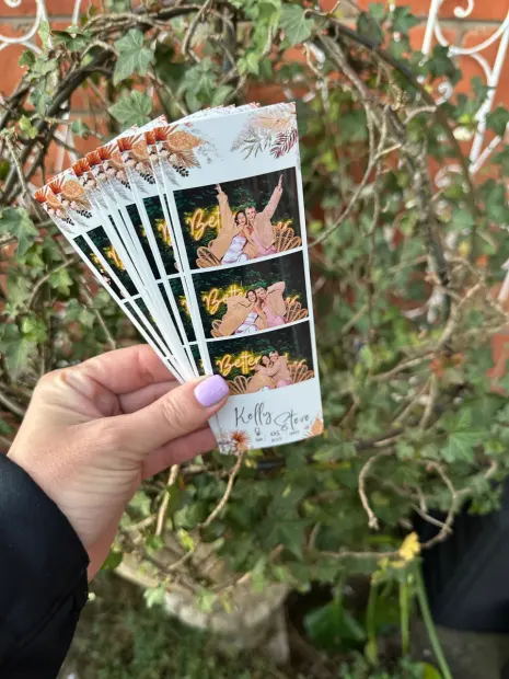 A fan of printed photostrips held up against the hedge at a Providence wedding