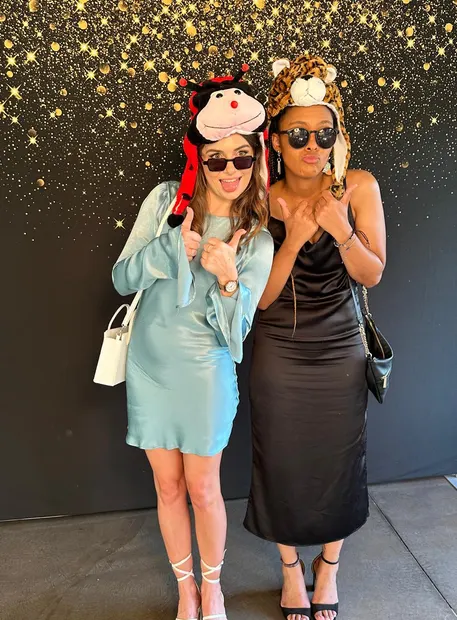 Two guests posing with props against the gold confetti backdrop at Sweet Home