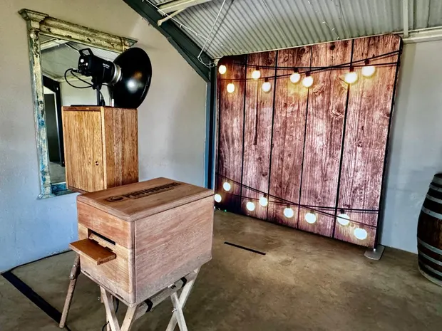 The photobooth and a lit timber backdrop beside a wine barrel at The Glades Farm