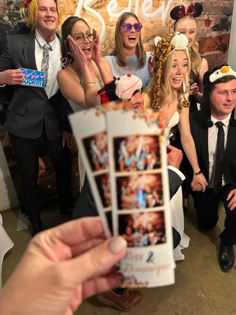 Wedding guests holding up their photostrip in front of the brick wall at The Groves