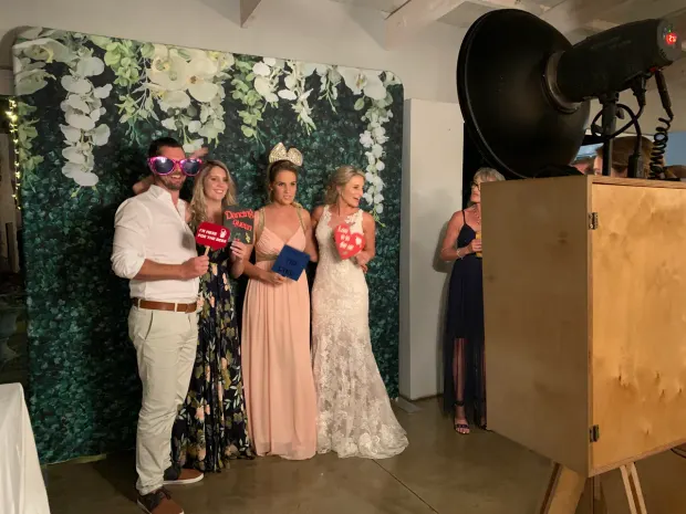 Wedding guests posing with props in front of the foliage wall at The Groves